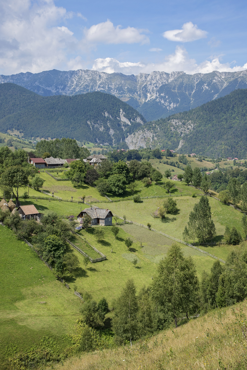 Green fields and scattered houses below a rugged mountain ridge near Măgura