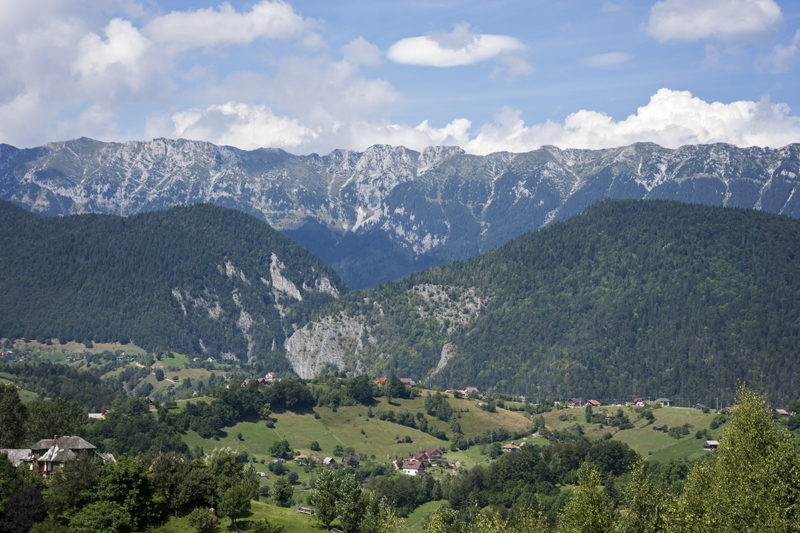 A pale rocky mountain ridge above forested slopes and green village fields