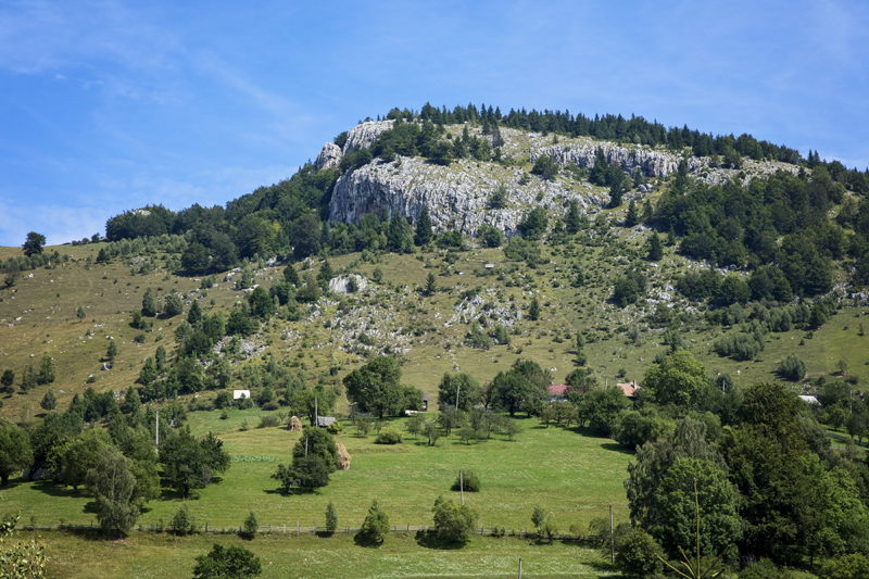 A rocky hilltop above green meadows, trees, and scattered rural houses