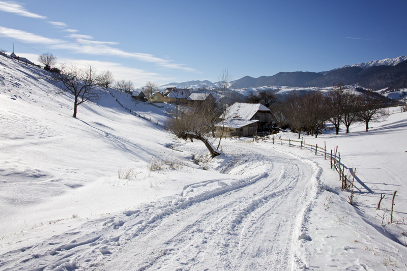 Tracks along a snow-covered lane passing wooden fences and village houses