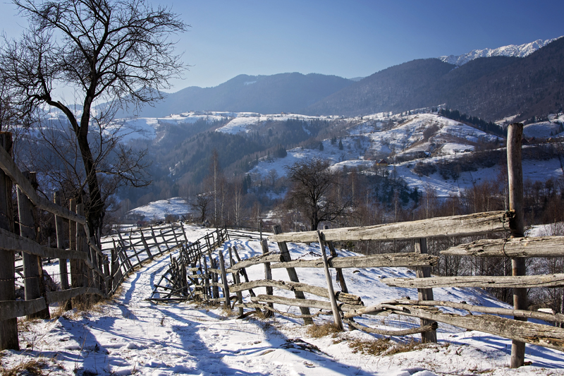 Wooden fences and bare trees overlooking a snow-covered valley and distant mountains