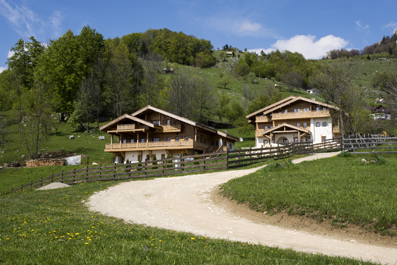 Samedru's wooden guesthouse buildings beside a curving gravel drive and green hillside