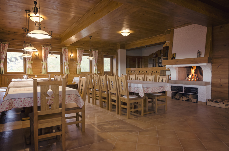 Wooden tables and chairs in Samedru's dining room, with ceiling beams and a brick fireplace